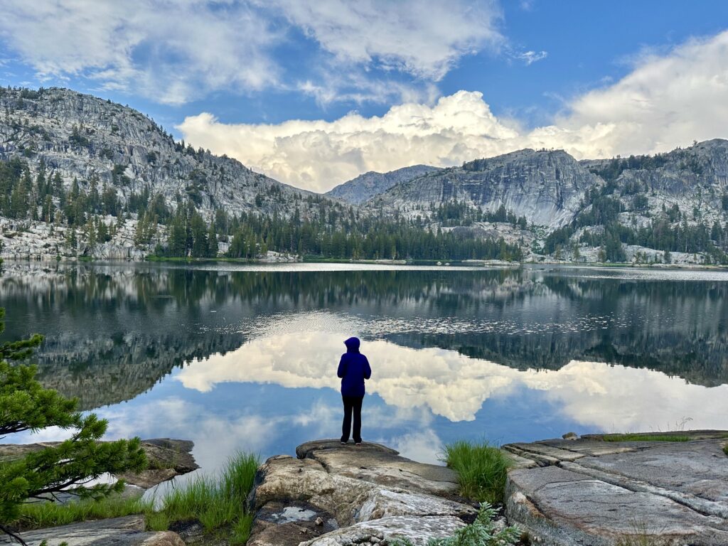 A hiker standing and looking at Smedberg Lake in Yosemite National Park. You will see this lake while hiking the Benson Lake Loop or the Pacific Crest Trail 